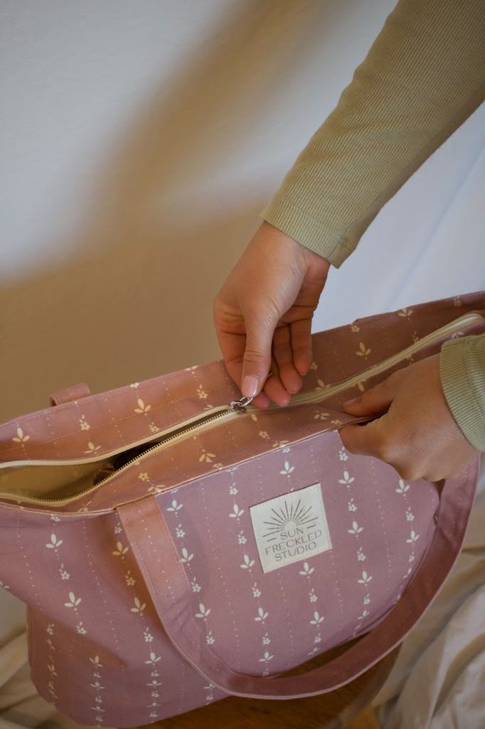 The full top zipper being closed on a pink floral Sun Freckled Studio tote bag.